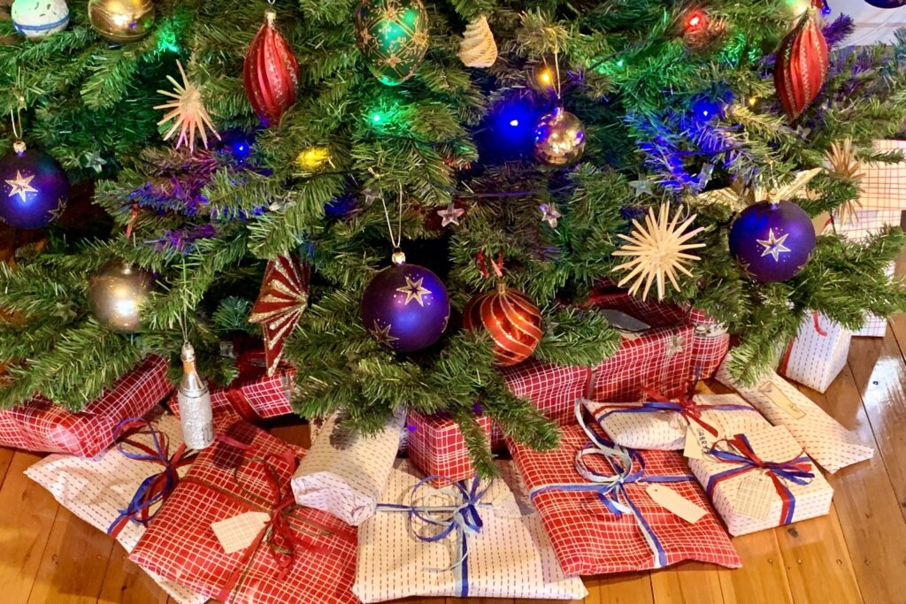 Weihnachtsbaum mit bunten Kugeln, darunter liegen viele verpackte Geschenke