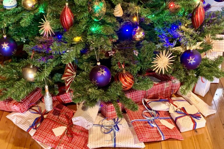 Weihnachtsbaum mit bunten Kugeln, darunter liegen viele verpackte Geschenke