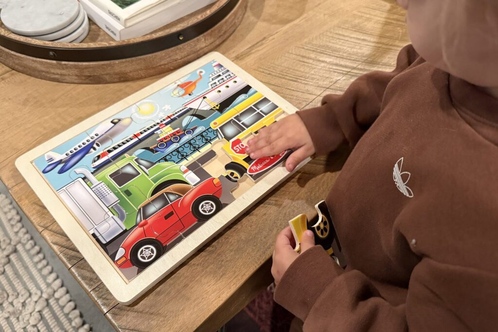 Kind setzt ein Teil in ein buntes Holz-Rahmenpuzzle mit Fahrzeugen ein