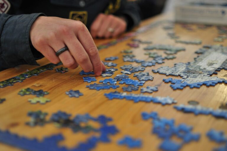 Hände legen blaue Puzzleteile auf einem Holztisch zusammen