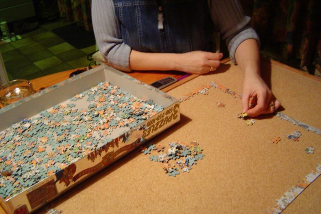 Eine Person sortiert Puzzleteile in einem Schachteldeckel neben dem begonnenen Puzzlerand