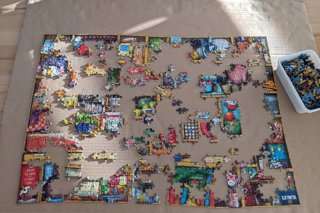 Angefangenes buntes Puzzle auf einer Unterlage mit einer Sortierbox voller Teile daneben