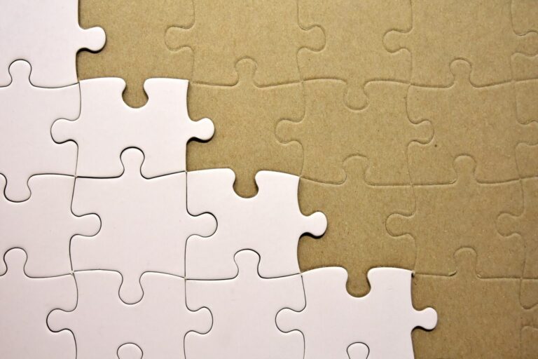 Weißes Puzzle, bei dem noch einige Teile fehlen und auf einer braunen Unterlage liegen