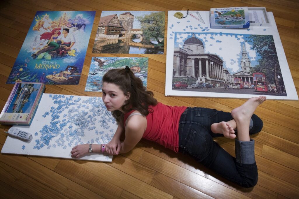 Junge Frau liegt auf dem Boden zwischen mehreren großen, fertig gelegten Puzzles