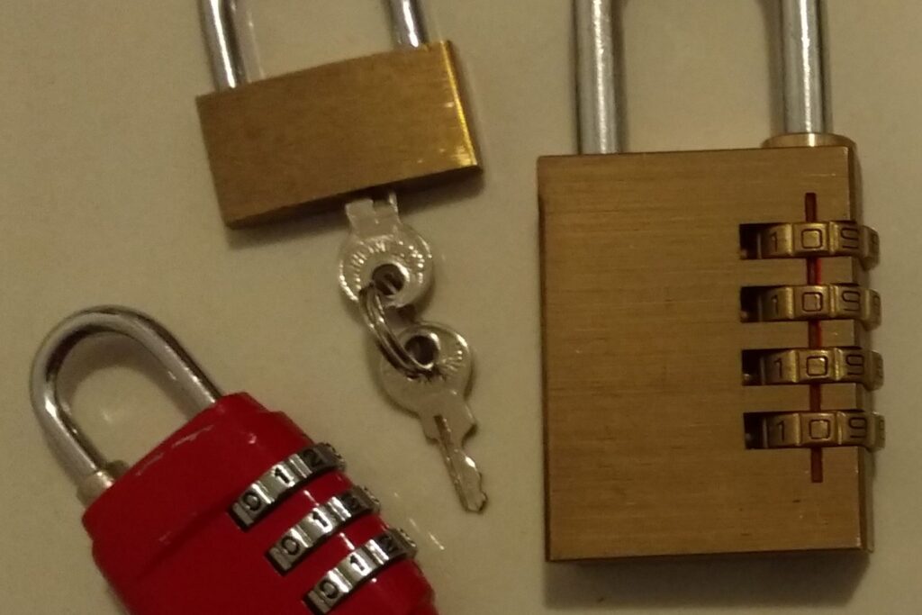 Drei Vorhängeschlösser, zwei davon mit Zahlenkombination, auf einem Tisch