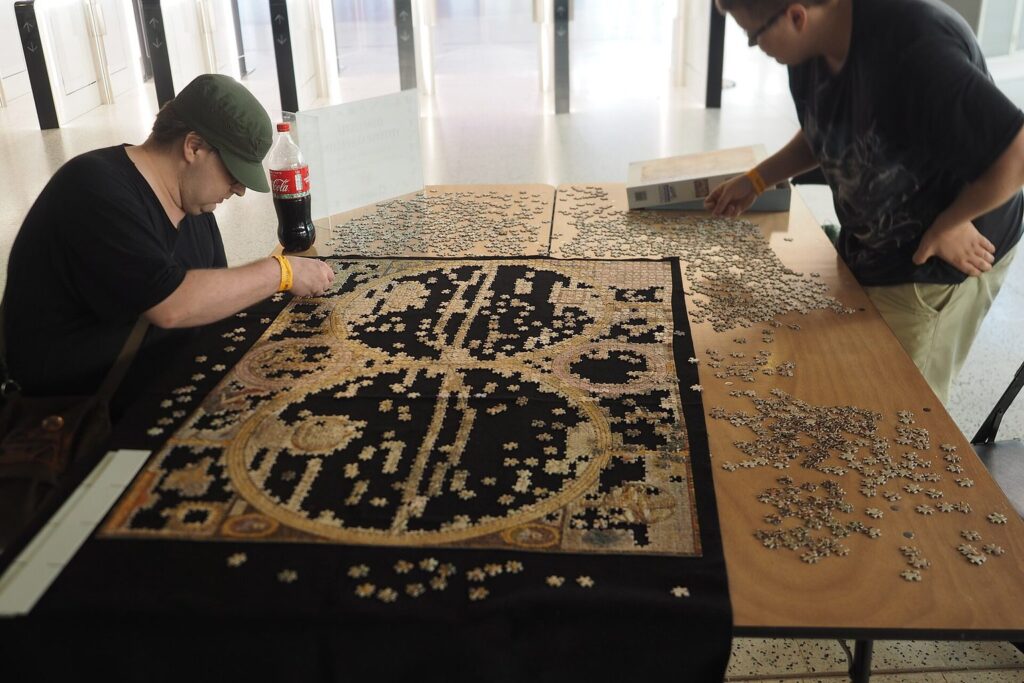 Zwei Personen arbeiten an einem Tisch gemeinsam an einem großen Puzzle